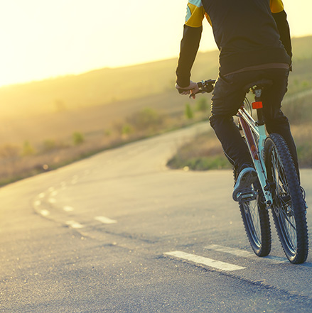 silhouette of a person riding a bicycle on a rural road at sunrise