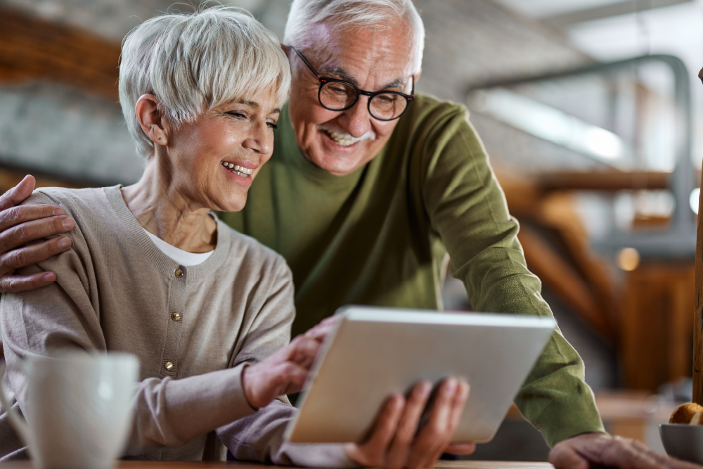 An older couple smiles while reading information on a website.